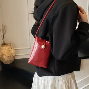 Glossy red patent leather mini crossbody bag with a large pearl button closure