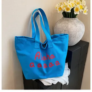 Détail d'un grand sac cabas en toile bleu ciel avec imprimé Aloha rouge sur bois