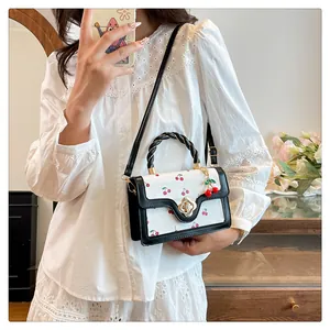 Detail of white crossbody bag with cherry print, braided handle and gold flower clasp
