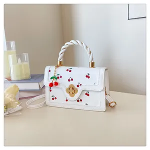 Close-up of white crossbody bag with red cherry prints and golden floral lock