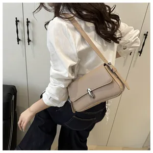 Detail of a beige leather shoulder bag with a sleek U-shaped silver buckle on a model