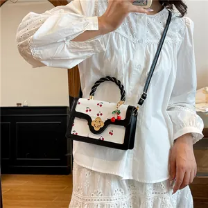 White crossbody bag with red cherry prints, black trim and gold flower clasp