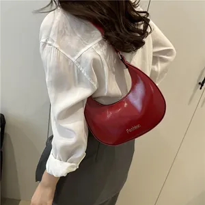 Sac à bandoulière demi-lune en cuir verni rouge avec nœud porté par un mannequin