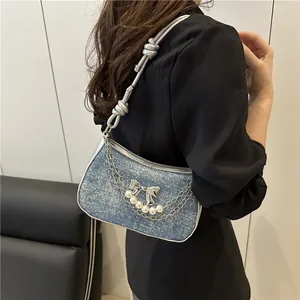Blue denim shoulder bag with silver chains, white pearls, and a bow charm accessory