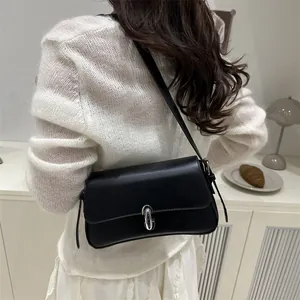 Minimalist black rectangular shoulder bag with silver oval metal lock worn by a model