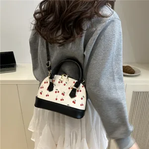 Trendy cherry print shell handbag with black leather straps shown on a model