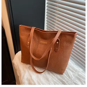 Detail of a brown tote bag featuring geometric embossed texture and FASHION metal plate
