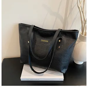 Detail of black PU leather tote bag with embossed letters and fashion label near book