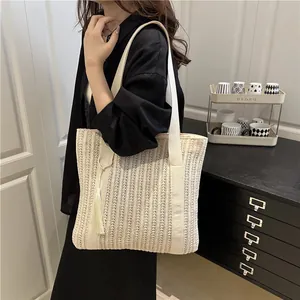 Handwoven beige straw tote bag with vertical stripes, long shoulder straps and tassel charm