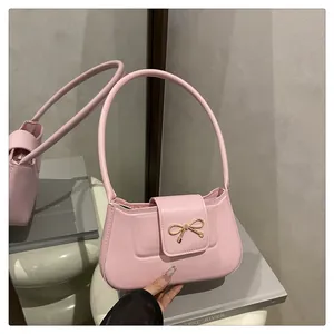 Détail d'un sac baguette en similicuir rose avec boucle nœud doré sur surface miroir