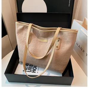 Close-up of beige tote bag with embossed letters and fashion brand plate in a gift box