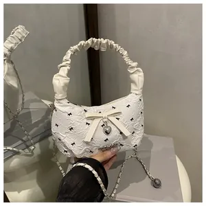 Detail of white pleated handbag with black bow prints and a silver heart pendant