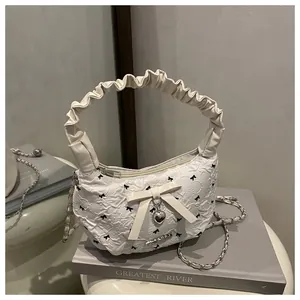 Macro detail of a pleated white hobo bag with bow prints and a heart-shaped metal pendant