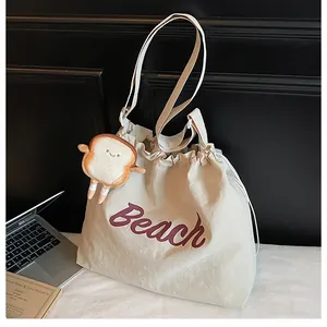 Detail of cream tote bag with Beach lettering and cute bread plush charm accessory