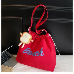 Detail of red canvas tote bag with blue Beach text and cute bread plush keychain