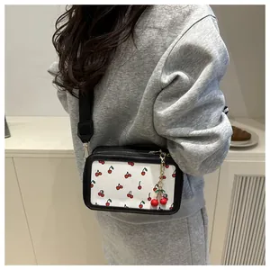 Detail of a white square crossbody bag with red cherry print and wide black strap
