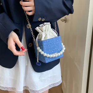 Blue denim bucket bag with pearl handle and drawstring detail worn on a shoulder