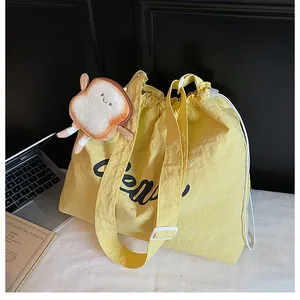 Detail of yellow canvas tote bag with adjustable strap, drawstring closure, and plush charm