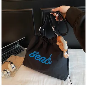 Detail of black tote bag with blue Beach print, drawstring closure and plush pendant