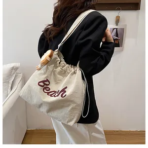 Detail of beige tote bag with Beach lettering and cute plush charm on wide shoulder strap