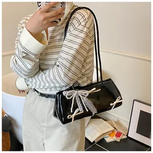 Detail of black glossy patent leather shoulder bag with lace bows and pearl charms