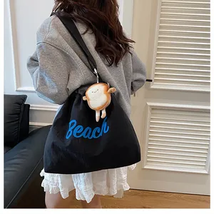 Detail of black canvas tote bag with blue Beach lettering and cute plush toast pendant