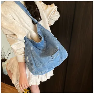 Close-up of light blue washed denim crossbody bag with distressed fringe and dual front pockets