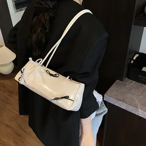 Creamy rectangular underarm bag with black bow, lace trim and pearl chain on a shoulder model