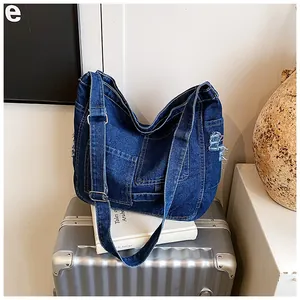 Detail of dark blue denim tote with distressed frayed edges and silver metal buckle