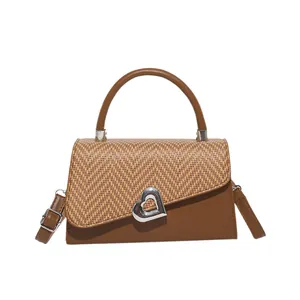 Brown leather and woven patchwork crossbody bag with silver heart buckle on white background