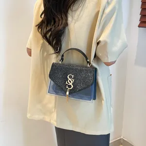 Sac bandoulière chic en PVC transparent avec logo S doré et pompon, porté par un mannequin
