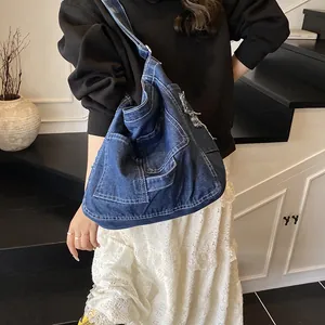 Large blue denim crossbody bag with contrast stitching and frayed edges on model