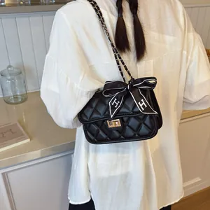 Black quilted chain shoulder bag with an elegant 'H' ribbon bow shown on a person