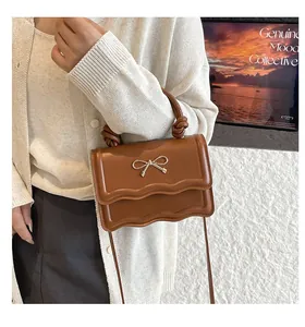 Close-up of dark brown handbag featuring a silver metal bow and wavy edge flap design