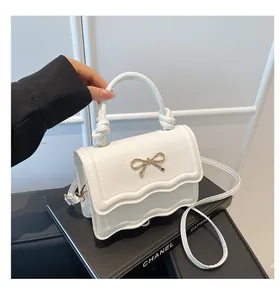 Detail shot of white bow shoulder bag with wave edge design and golden metal bow