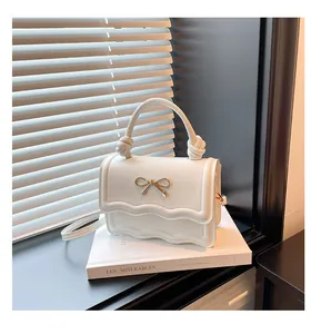 Detail of white glossy mini bag with wavy flap, gold bow accent and knot handle detail