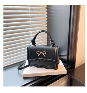 Detail of black mini crossbody bag featuring a wavy flap and golden bow ornament
