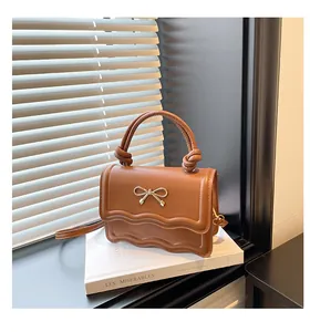 Detailed view of caramel leather handbag featuring wavy flap and golden bow buckle