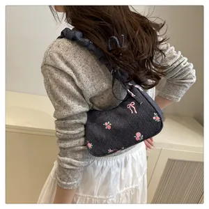Detailed embroidery of pink roses and bows on a blue denim pleated shoulder bag