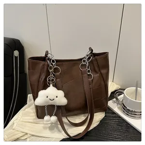 Detail of dark brown tote bag with geometric texture, silver chain, and plush cloud charm