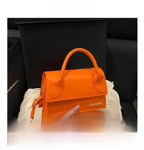 Detail view of mini orange leather crossbody bag featuring gold hardware and logo