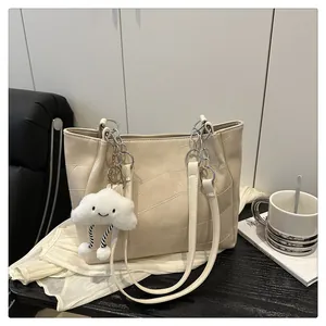 Detail of cream tote bag with patchwork texture, chain strap, and cloud charm