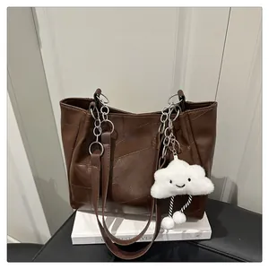 Detail of dark brown patchwork tote bag with metal chain handle and plush charm