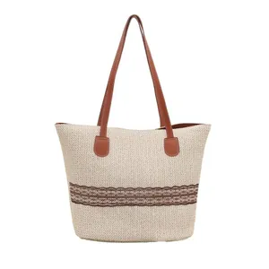 Straw tote bag with brown lace trim and faux leather handles shown on white background