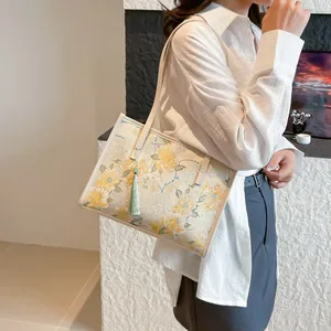 Large capacity floral embroidered shoulder bag with tassel shown on model in studio
