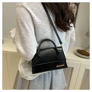 Close-up of a black matte leather mini crossbody bag featuring golden logo and top handle