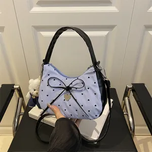 Striped hobo bag with black heart prints, bow detail, and plush bear charm on a chair