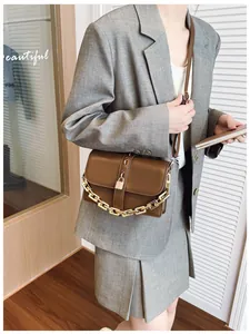 Detail of dark brown leather crossbody bag with chunky gold chain and metal buckle