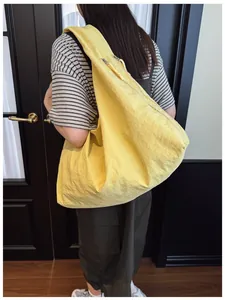 Detail of a bright yellow oversized nylon tote bag with crescent shape and zipper