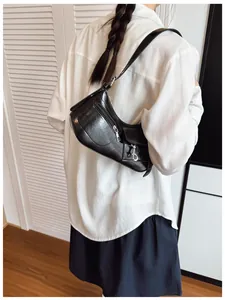 Detail of a black glossy underarm bag with zipper and buckle pockets shown on model